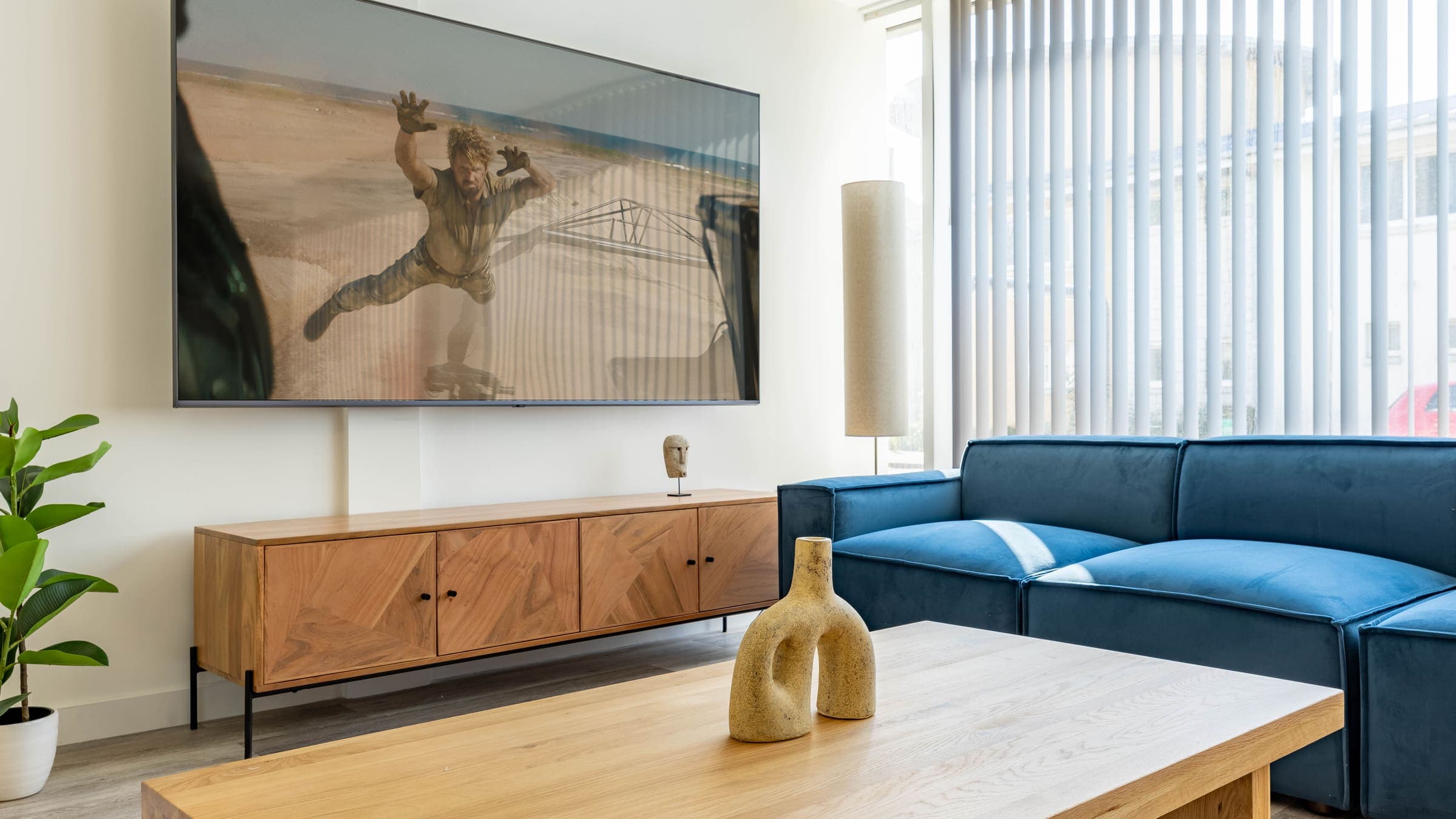 The common room at ABeleven, with a blue modular sofa, a low wooden table and a wall-mounted television
